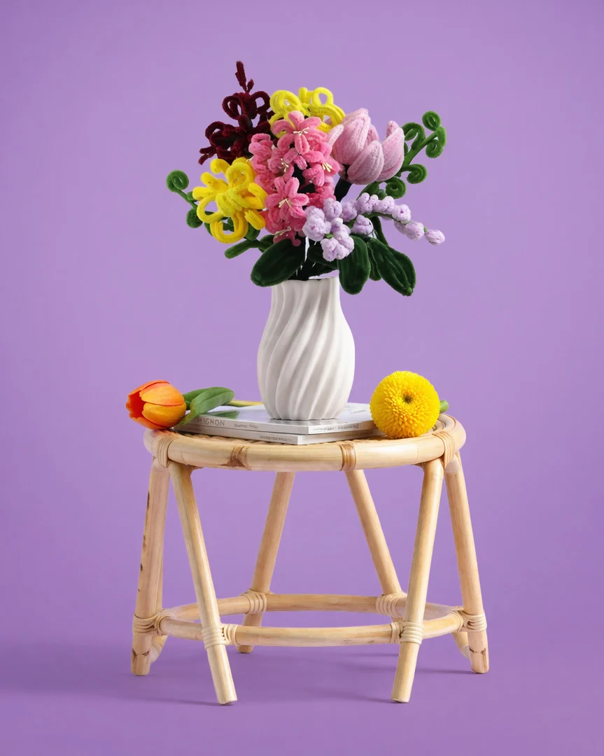 Bunter Blumenstrauß in weißer Vase auf einem runden Rattanstuhl mit Büchern