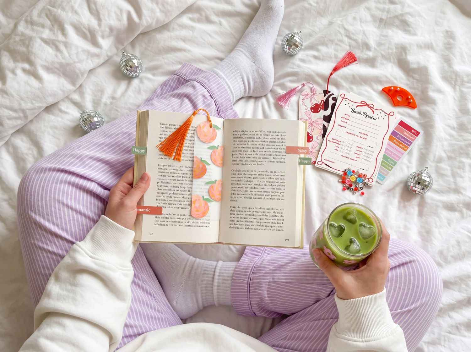 Eine Person hält ein geöffnetes Buch und ein grünes Getränk. Auf dem Bett liegen Bastelmaterialien